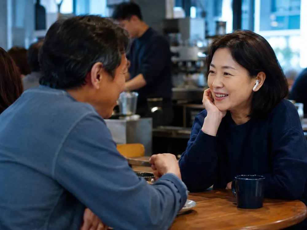 にぎやかなカフェでイヤホンをつけて向かいの相手と会話する様子